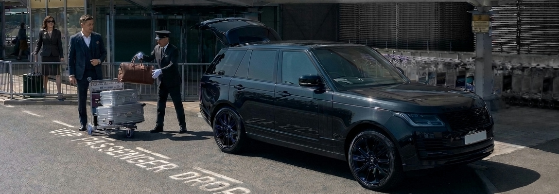 Chauffeur loading luggage into a black luxury SUV at an airport drop-off